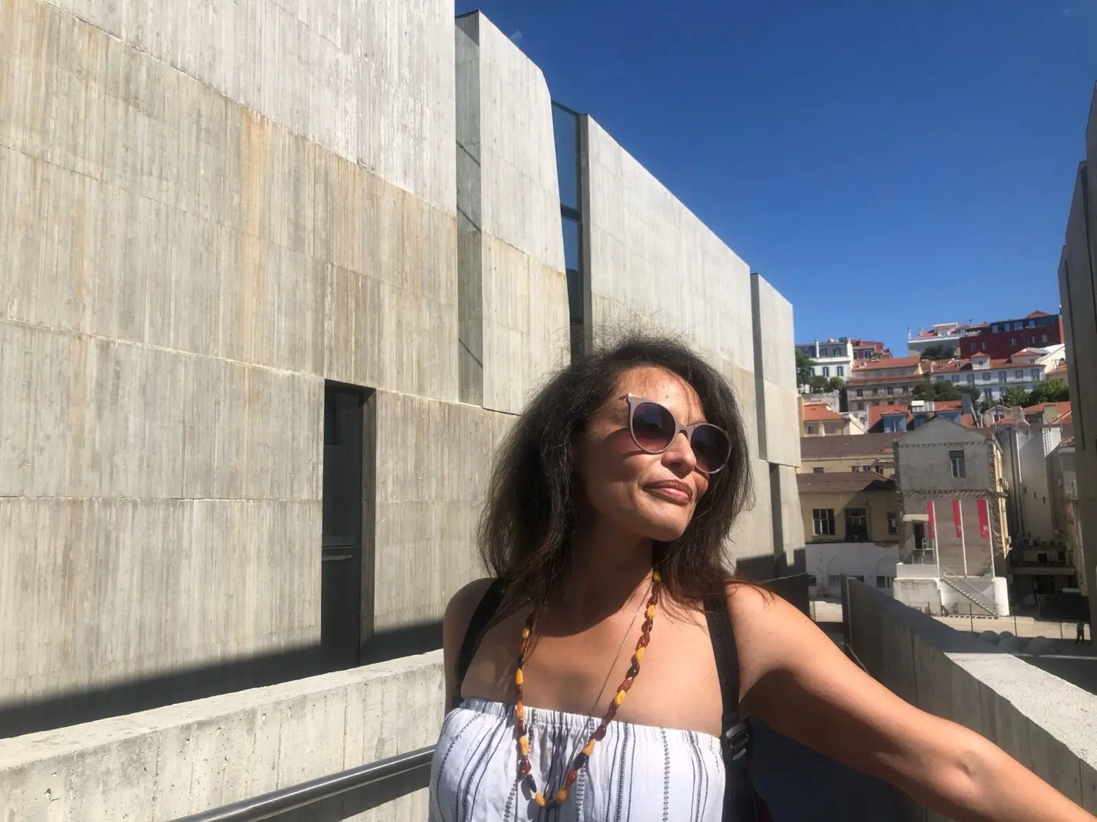 Ines in sunglasses, smiling in the sun against a concrete wall