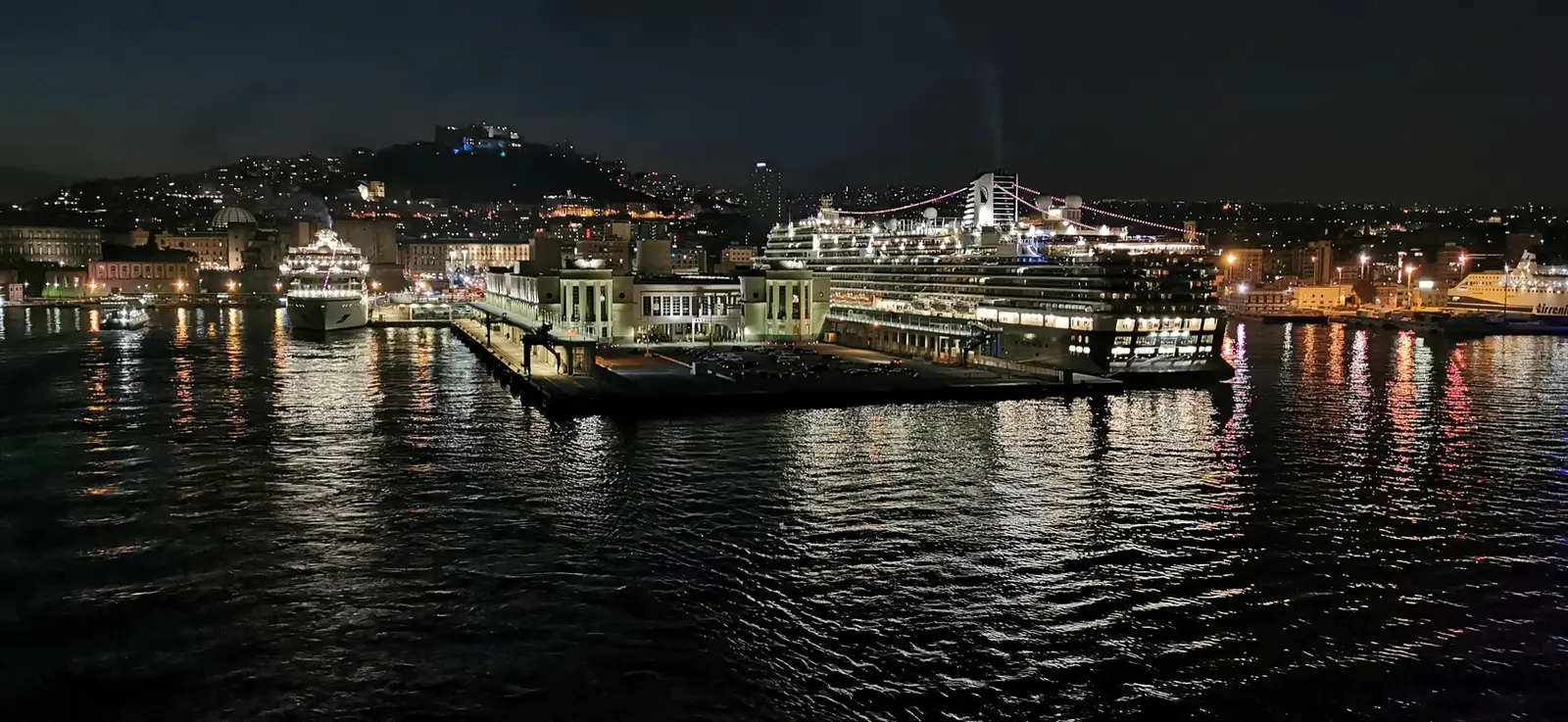 Naples harbour at night, the city lights reflected in the water and Castel Sant'Elmo lit on the hill