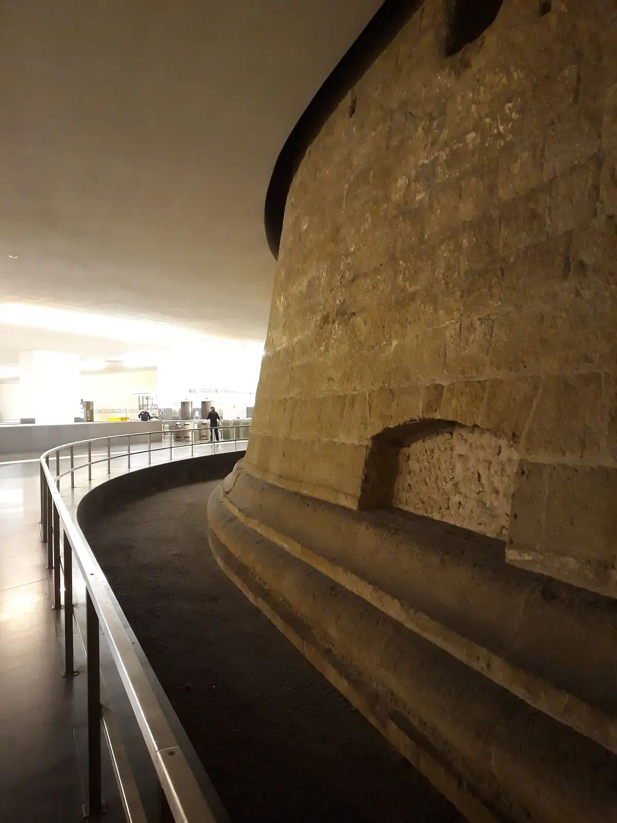 A curving walkway beside the massive stone base of a medieval tower inside Municipio station